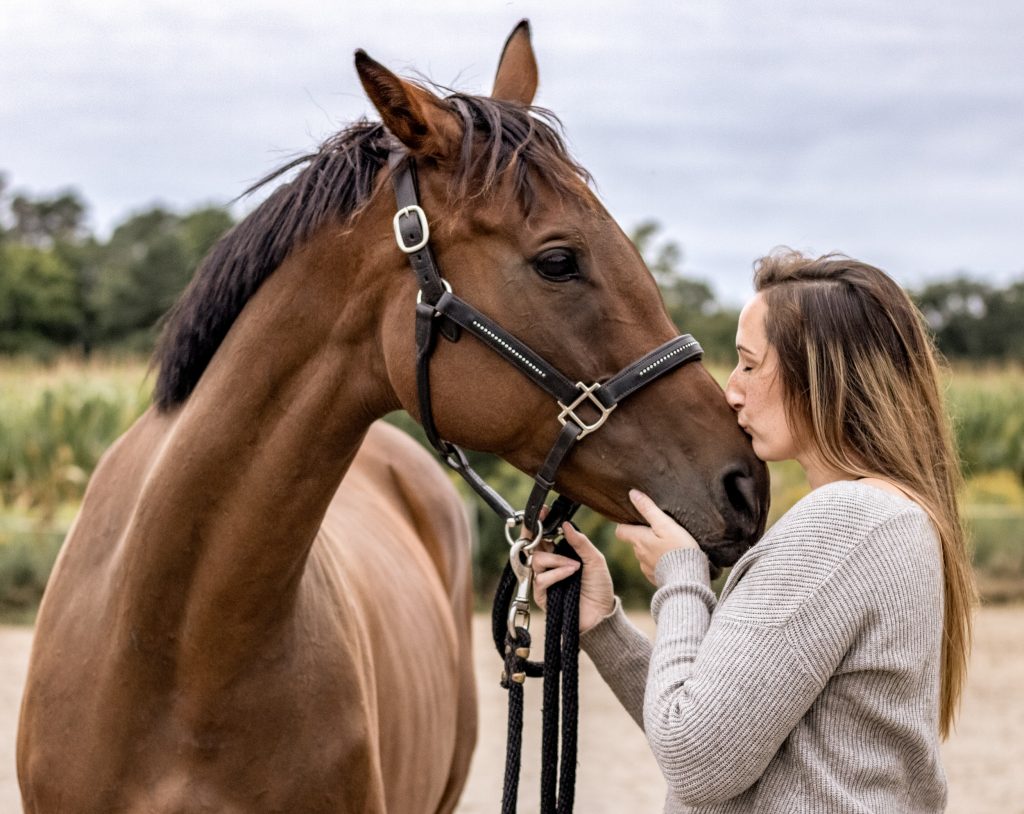 Justine Pitcher in a field, gently kissing the snout of her brown horse named Candy